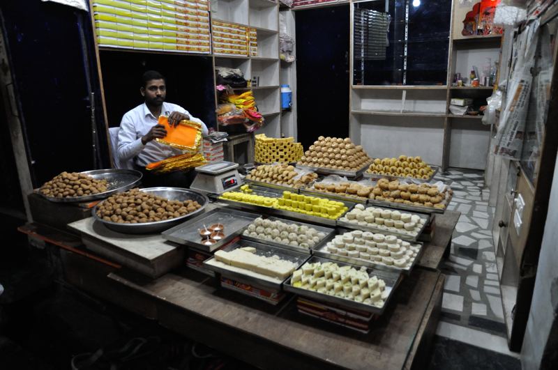 Mithai ki dukaan mein trays mein saji mithai aur dukaandaar